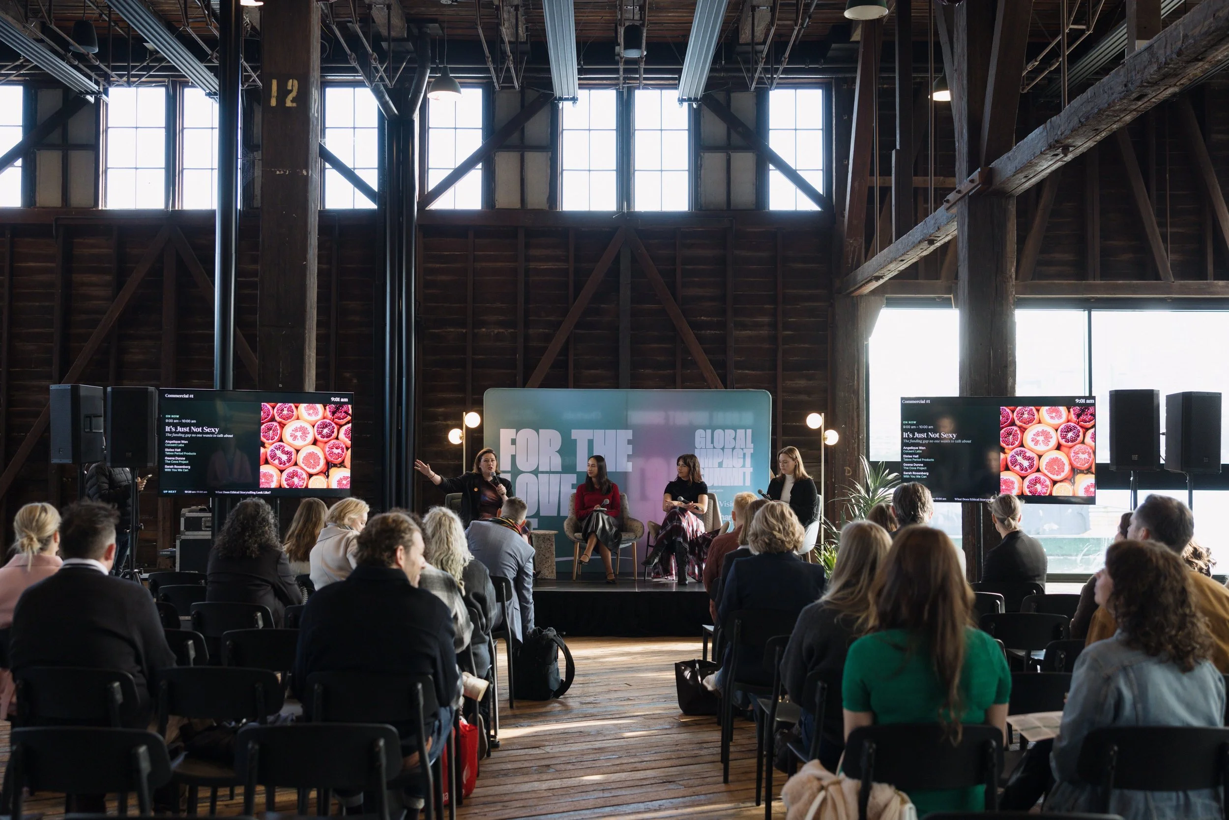 A panel on stage in a timber-beamed harbourside venue, audience in the foreground