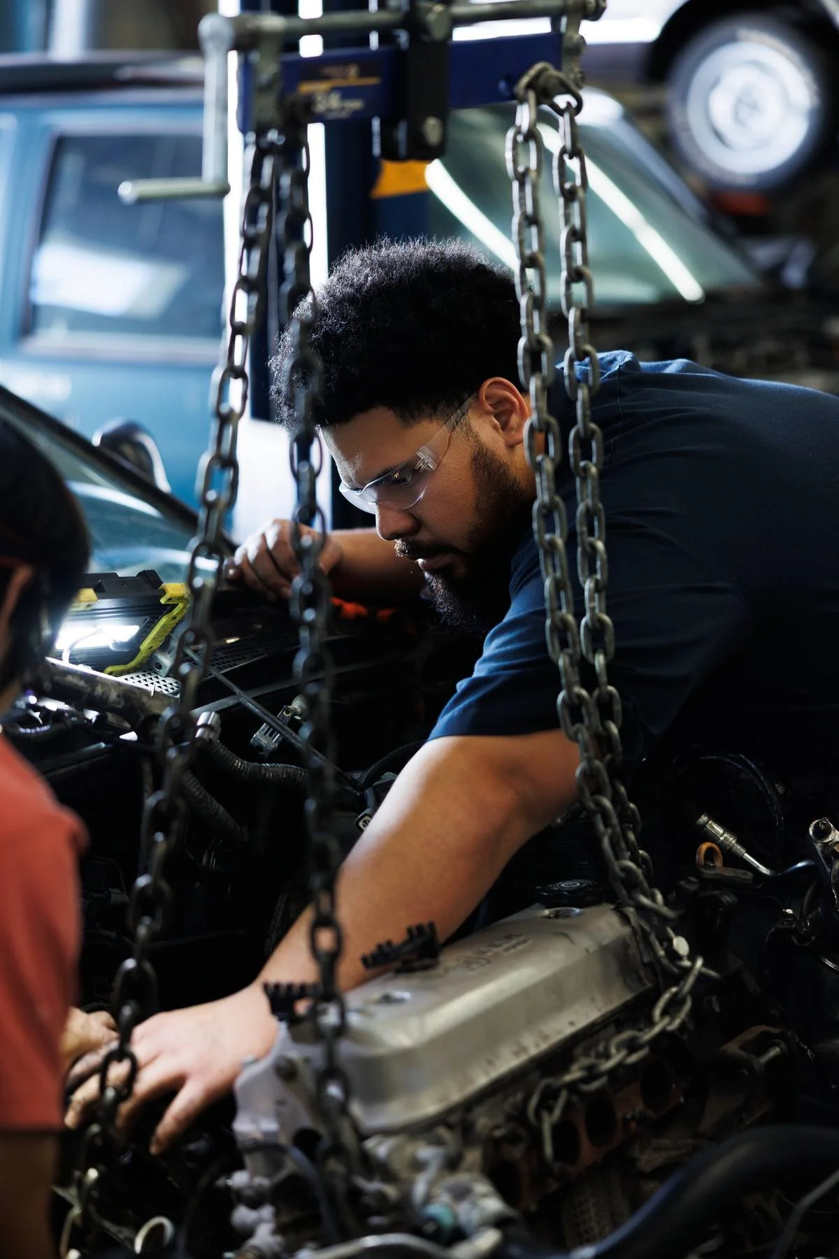 A student performs hands-on engine repair while working on a vehicle.