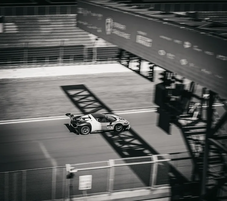 A race car caught in the shadow of a gantry, black and white