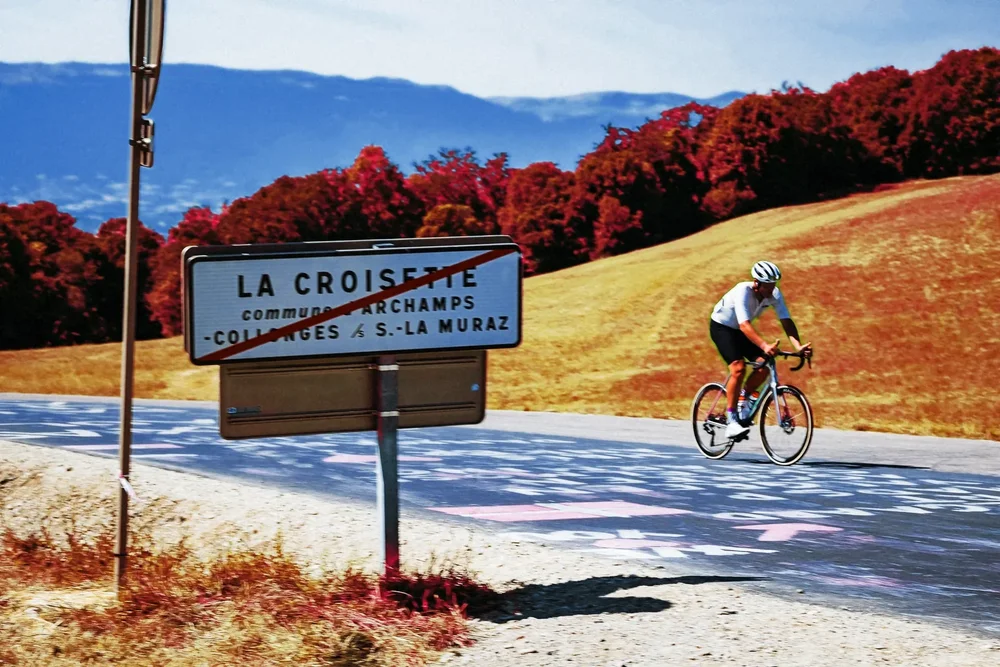 James riding past the La Croisette sign, the meadow behind him turned pink