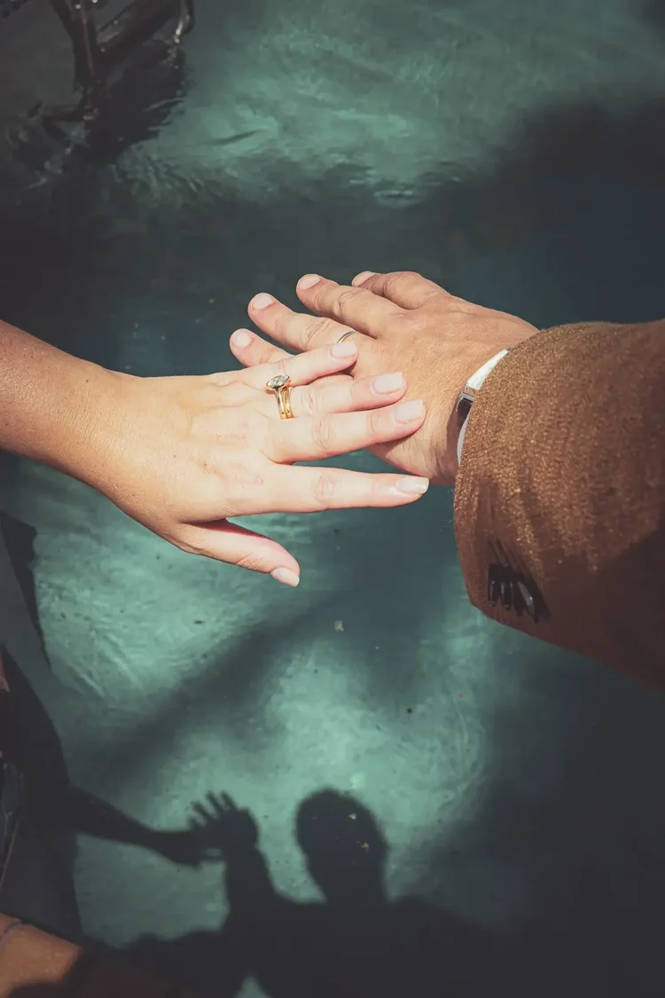 The couple's hands and wedding rings over pool water, their shadows on the surface below