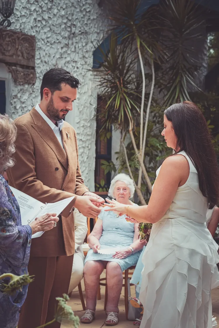 Simon placing the ring on Laura's finger during their courtyard wedding ceremony