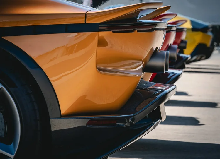 The rear of an orange sports car, more tail sections behind
