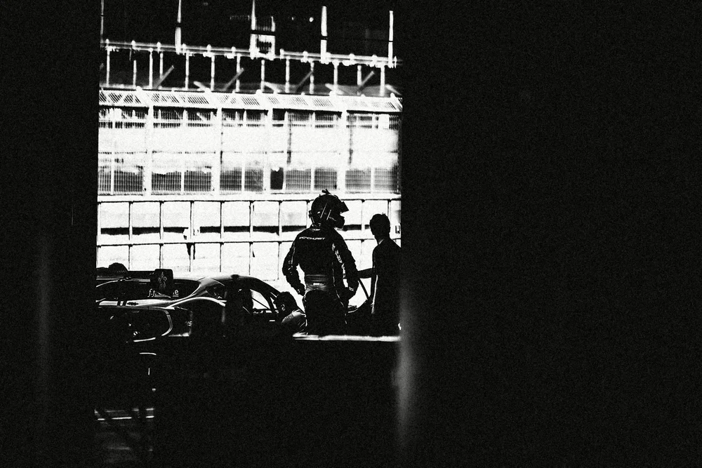 A driver framed in a garage doorway against the grandstand, grainy black and white