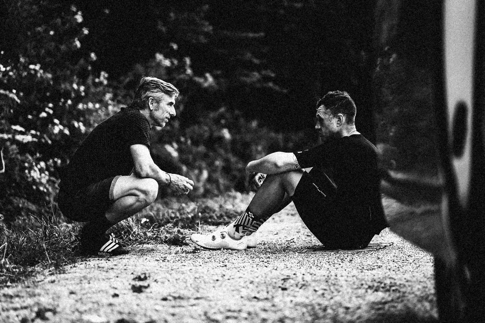 James and his support crew crouched by the roadside talking, grainy black and white