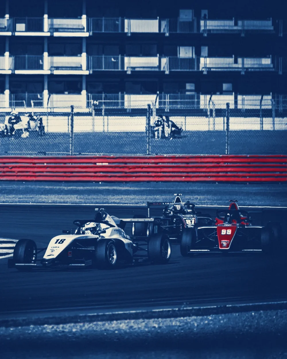 Three single-seaters in a line below the grandstand, cyanotype blue with the red car and barrier overprinted