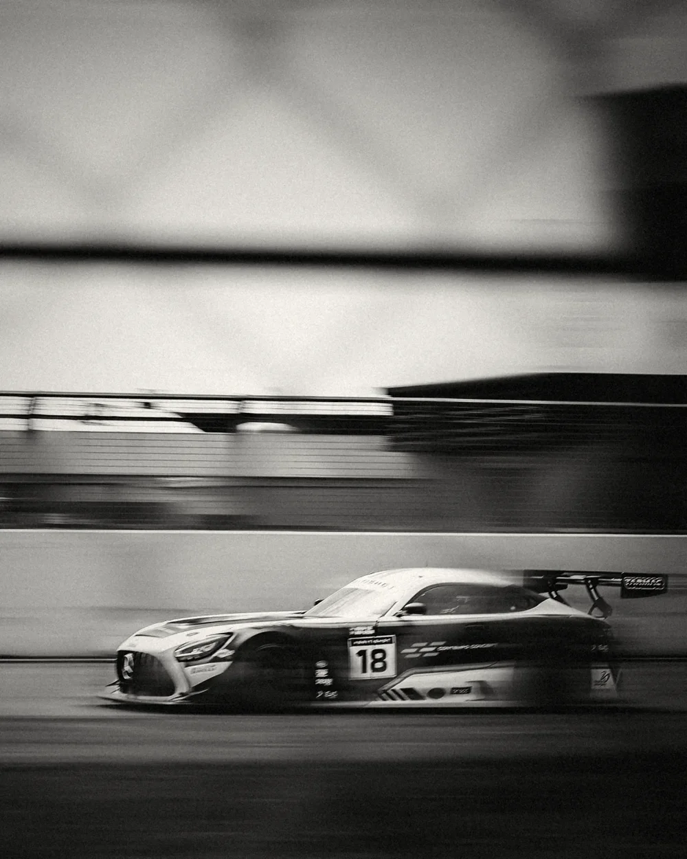 The number 18 Mercedes seen through the fence, background streaked, silver black and white