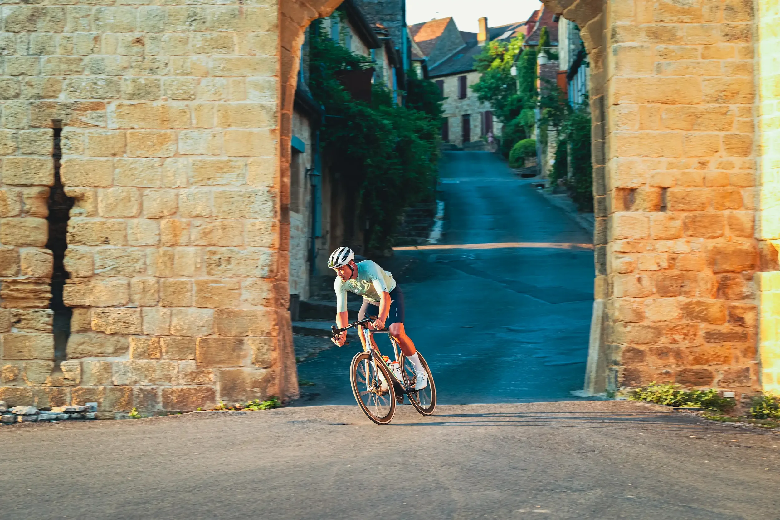 Cyclist riding through a stone archway into a French village on the 2026 Tour de France route