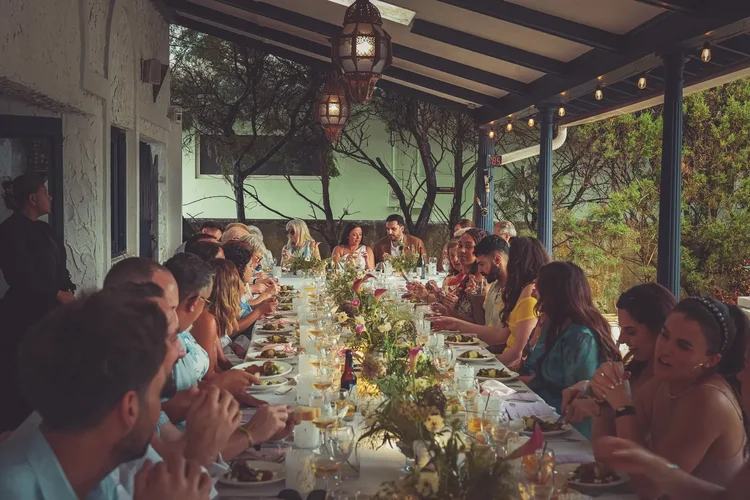 Wedding guests at a long table under a pergola with Moroccan lanterns, festoon lights and wildflowers