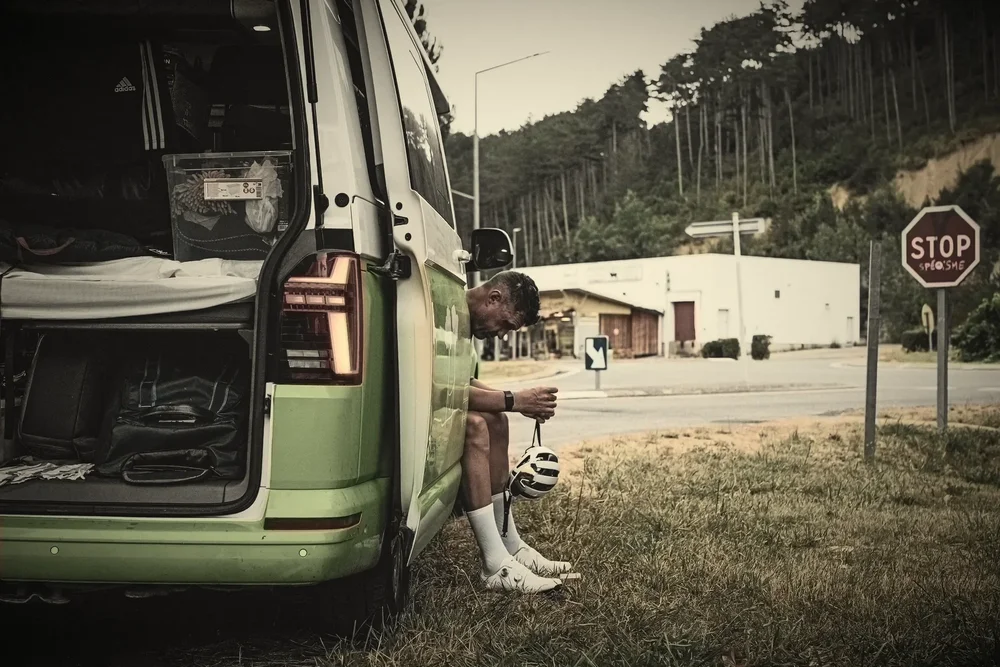 James resting against the green support van by a stop sign, hand-tinted black and white