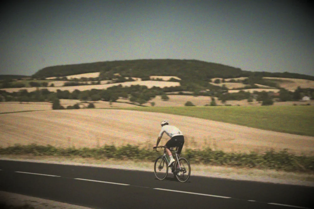 James riding past rolling harvested fields, muted Autochrome colour with a fine dye speckle