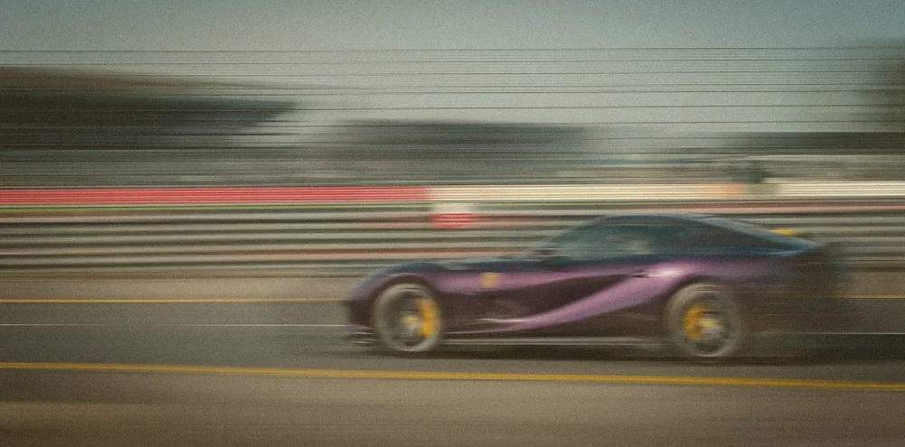 A purple sports car dissolving into motion blur past the grandstands