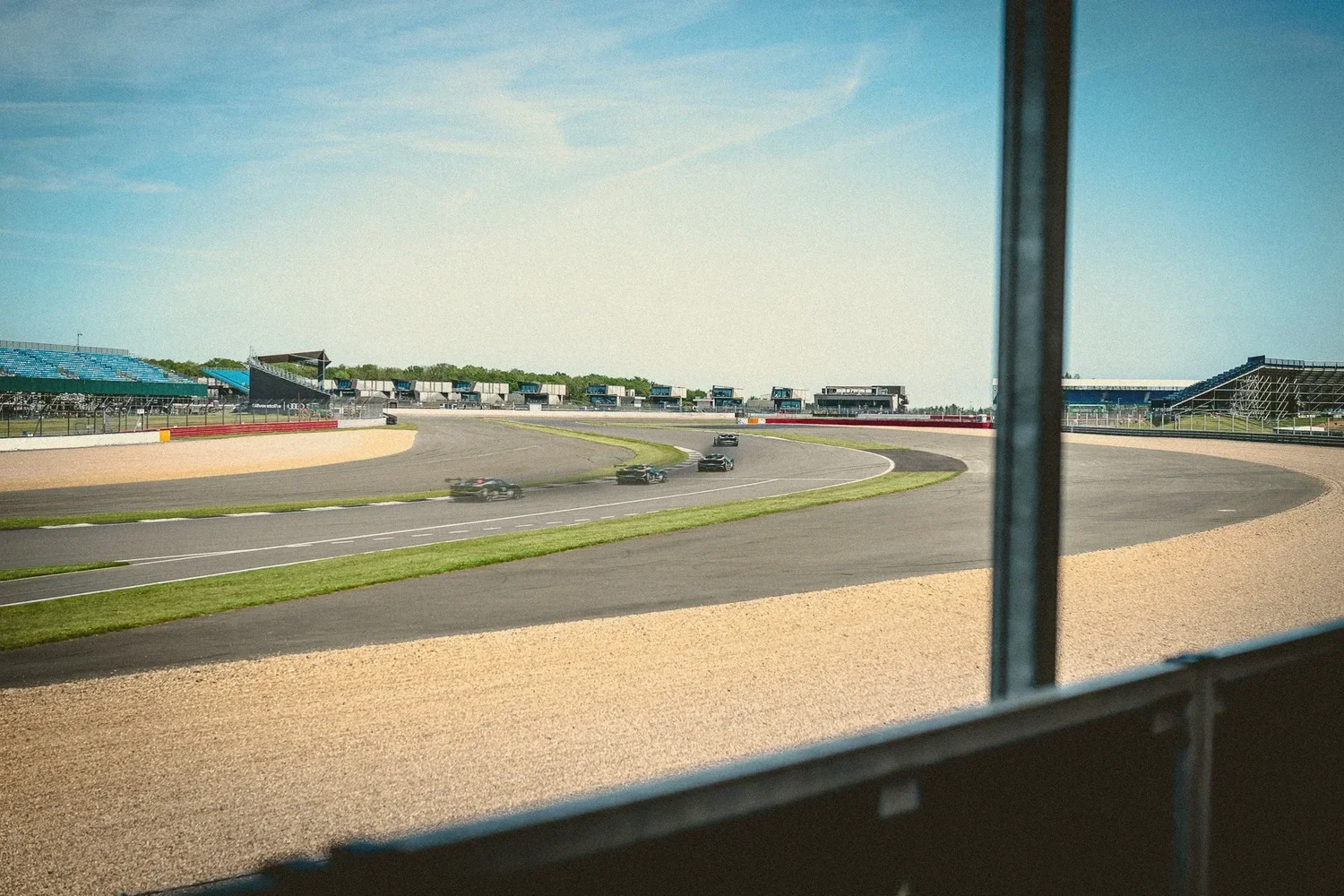 A race car shown at four points through a Silverstone corner in one image, ghosted then solid, seen through a spectator window