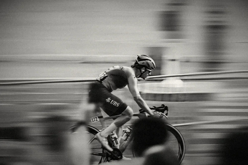 A rider close up at speed, the barrier and crowd pulled into motion, black and white