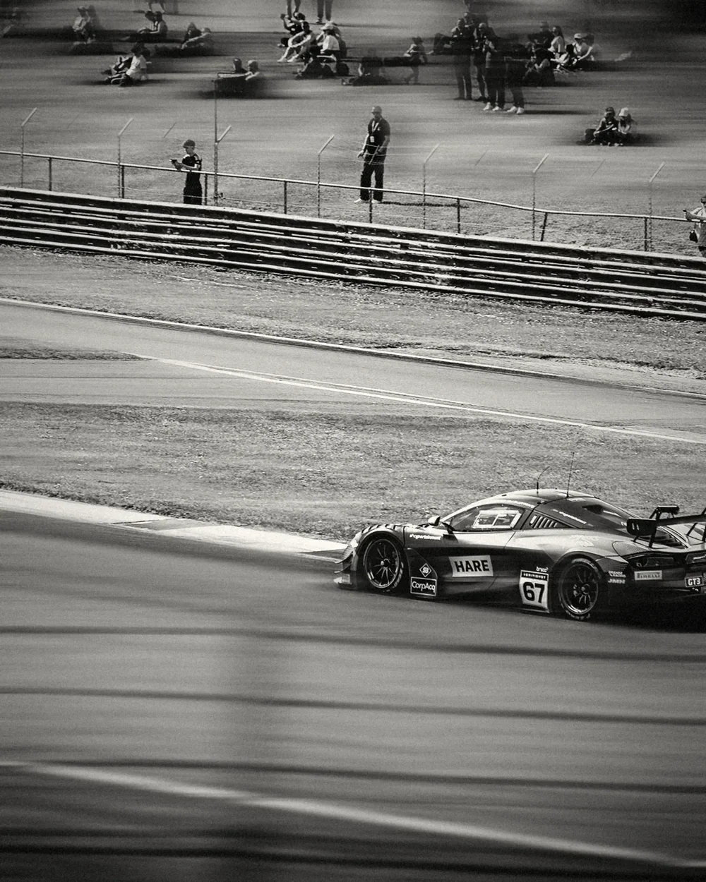 A McLaren on the far side of the circuit below the spectator bank, black and white with motion lines