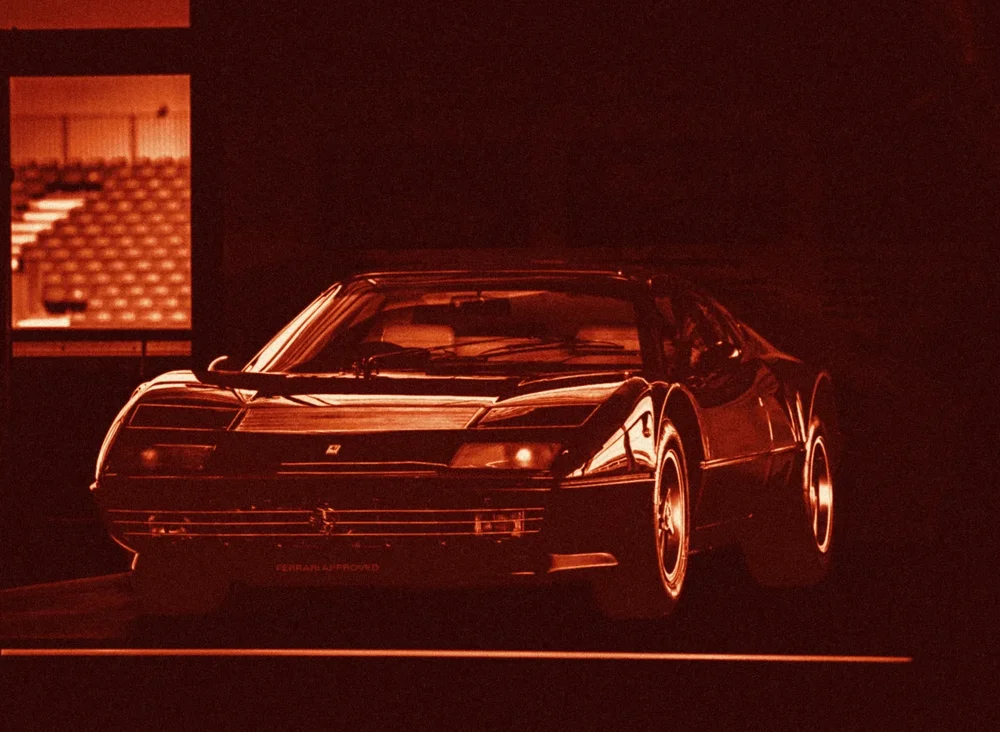A classic sports car emerging from a dark garage, toned deep red