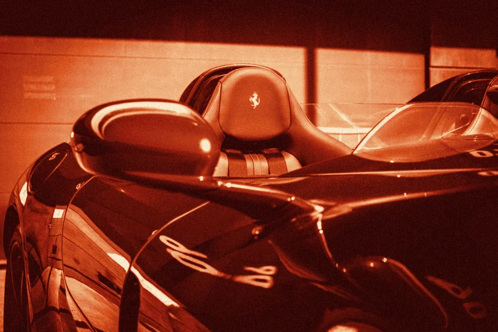 A red open-top sports car with a stitched horse on the seat, toned red and cream