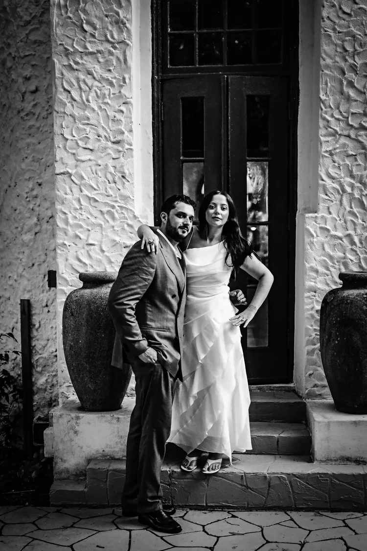 Black and white portrait of the couple by the villa's front door between two tall urns