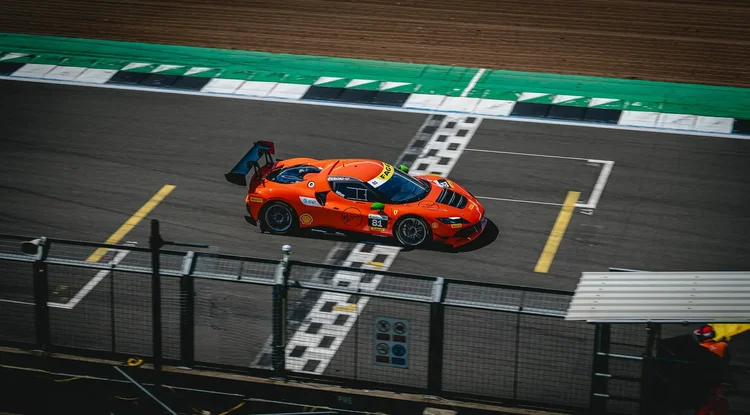 An orange race car crossing the chequered start line from above
