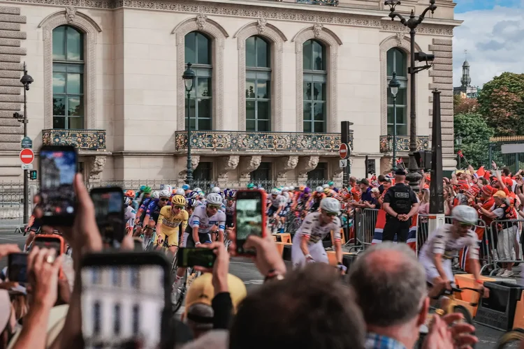 UAE Team Emirates leading the peloton through a corner in Paris as the crowd films on their phones, Tour de France 2026 final stage