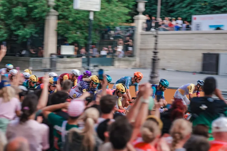 Panning shot of the peloton racing past raised hands and phones in Paris, Tour de France 2026