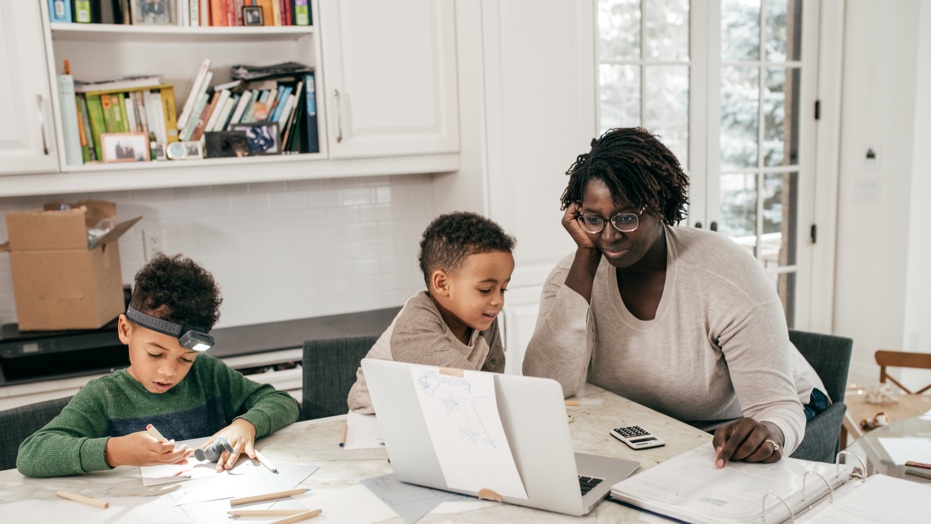 Homeschool mom working at laptop with two boys