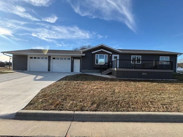 Spacious Rancho 6 exterior with dark grey siding, a large elevated wooden deck, and a two-car garage at Pinoy Ranch in Wagner, SD.
