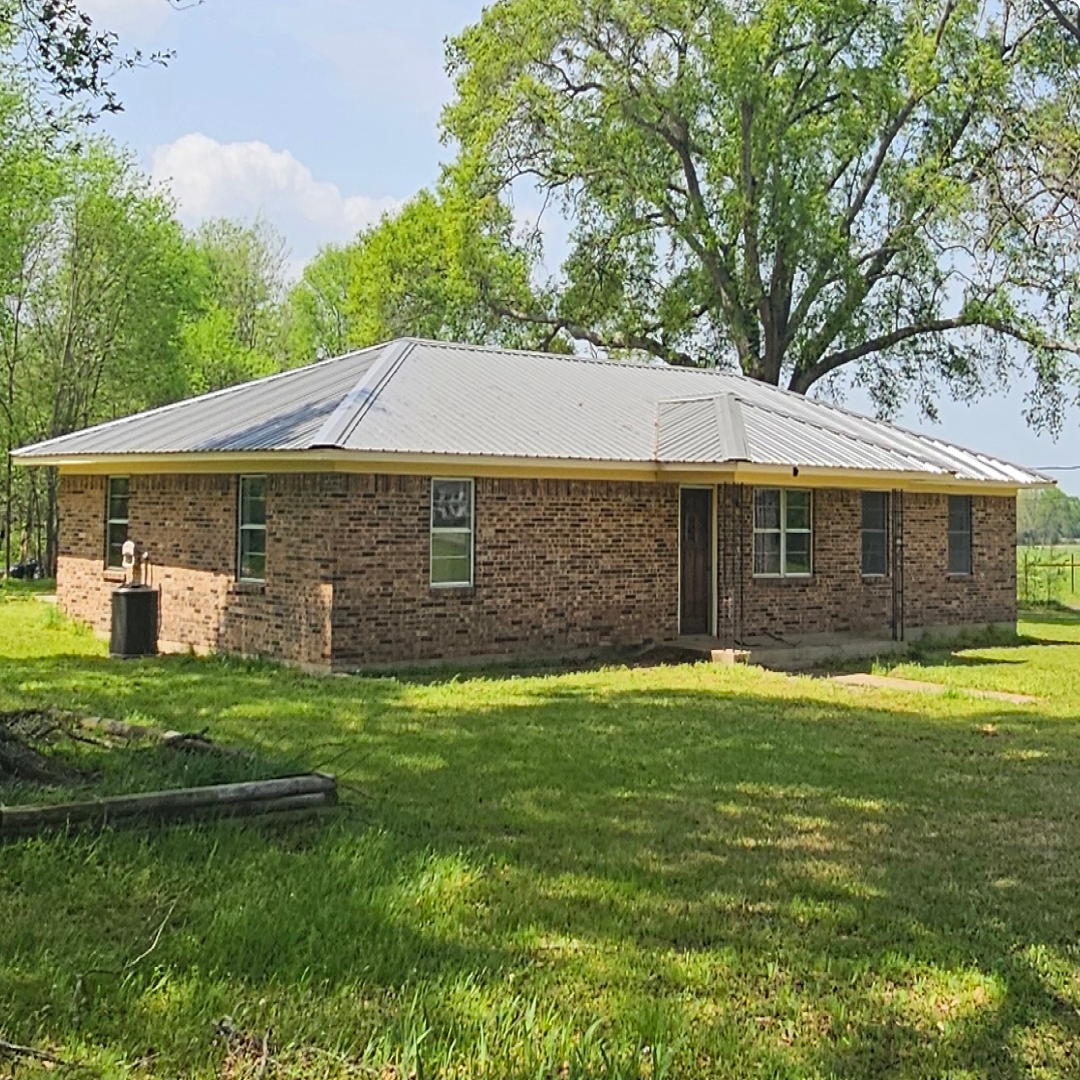 Modern brick exterior of Rancho 4 at Pinoy Ranch with a silver metal roof and lush green lawn in Canton, TX.