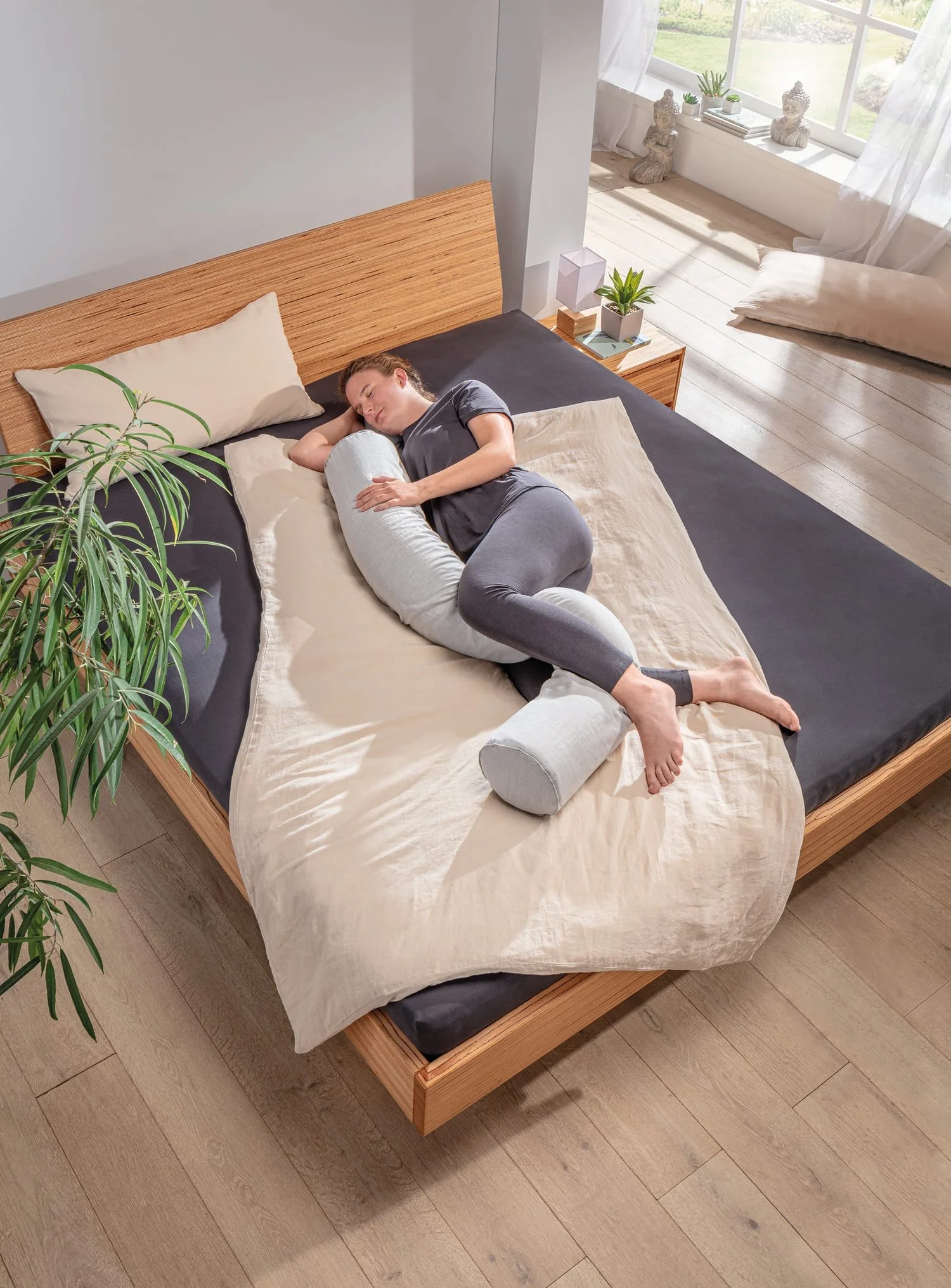 Woman sleeping on her side hugging a long natural latex bolster between her knees
