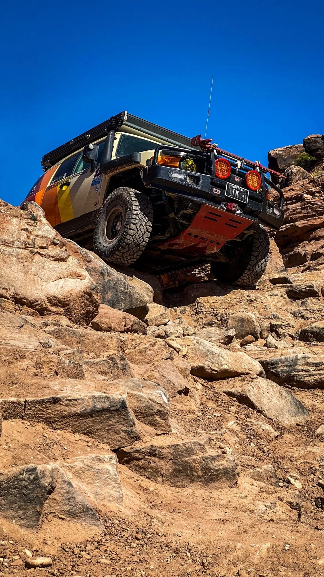 Striped FJ Cruiser climbing a red rock ledge under a blue sky on a spring road trip through Utah