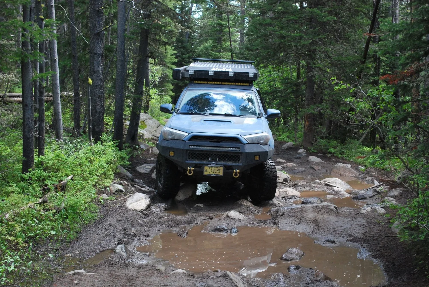 Silver 4Runner driving through a muddy puddle on a forest trail on the North Meadow Creek Twin Lakes trail in the Tobacco Root Mountains, Montana