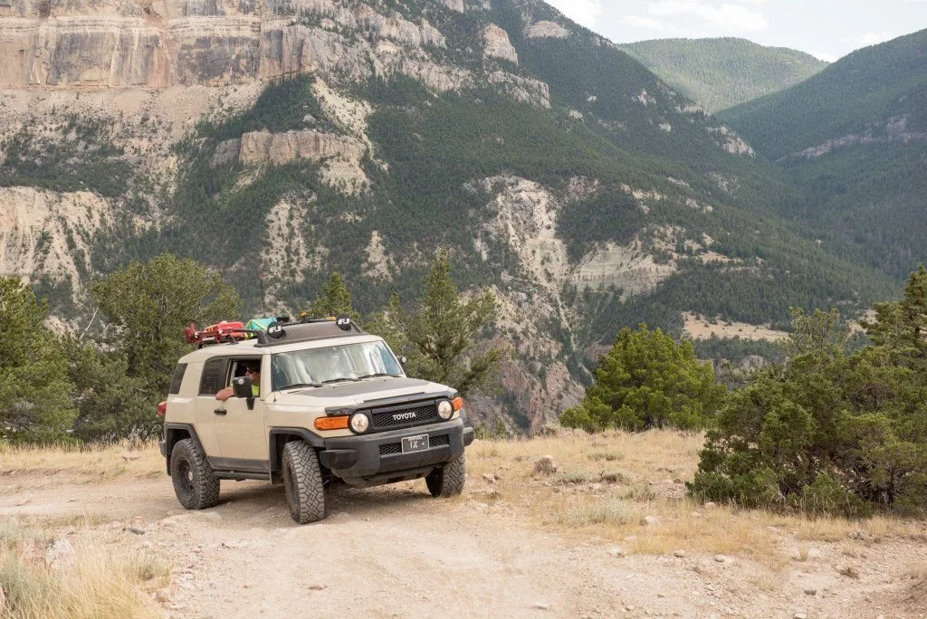 Tan Toyota FJ Cruiser on a dirt road with the cliffs and forested walls of Clarks Fork Canyon behind on the Morrison Jeep Trail in Clarks Fork Canyon near Cody, Wyoming