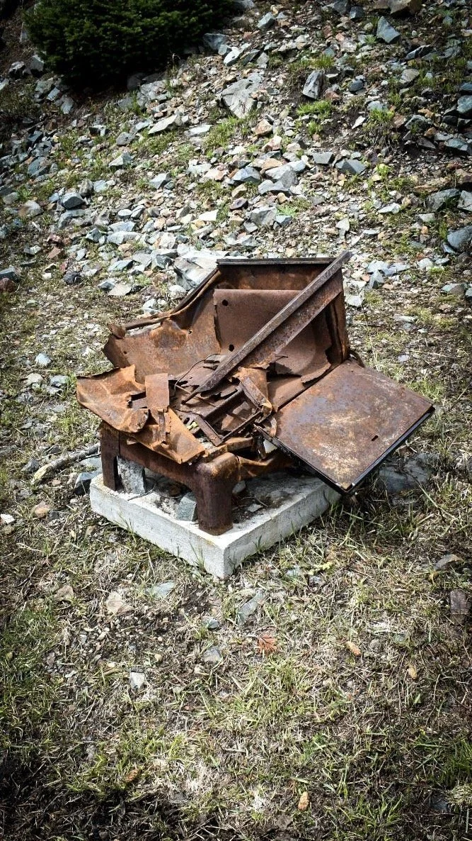 Rusted iron mining equipment sitting on a concrete base in the grass in the Elkhorn Mountains near Boulder, Montana