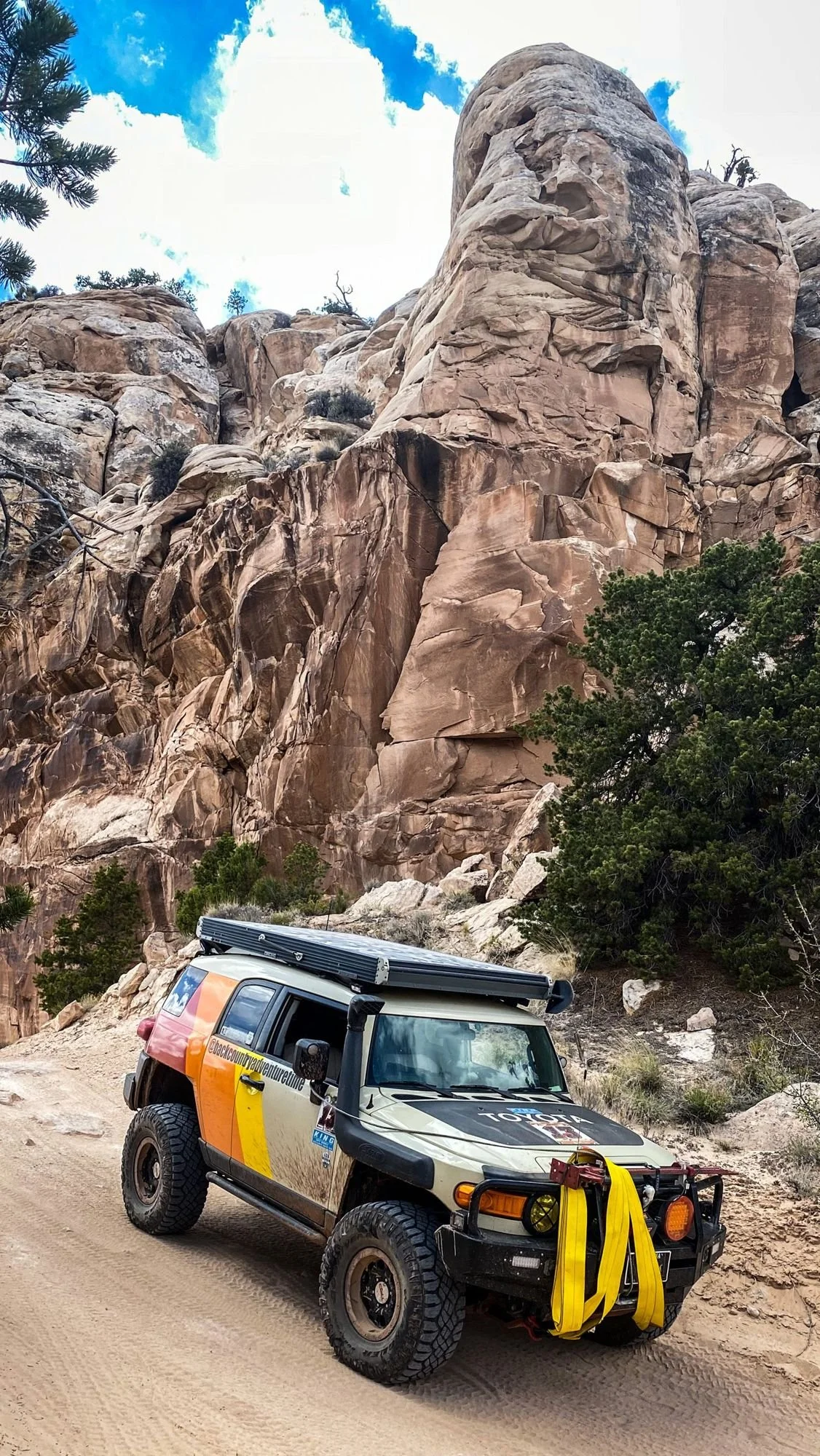 Striped FJ Cruiser driving below tall sandstone towers on a spring road trip through Utah