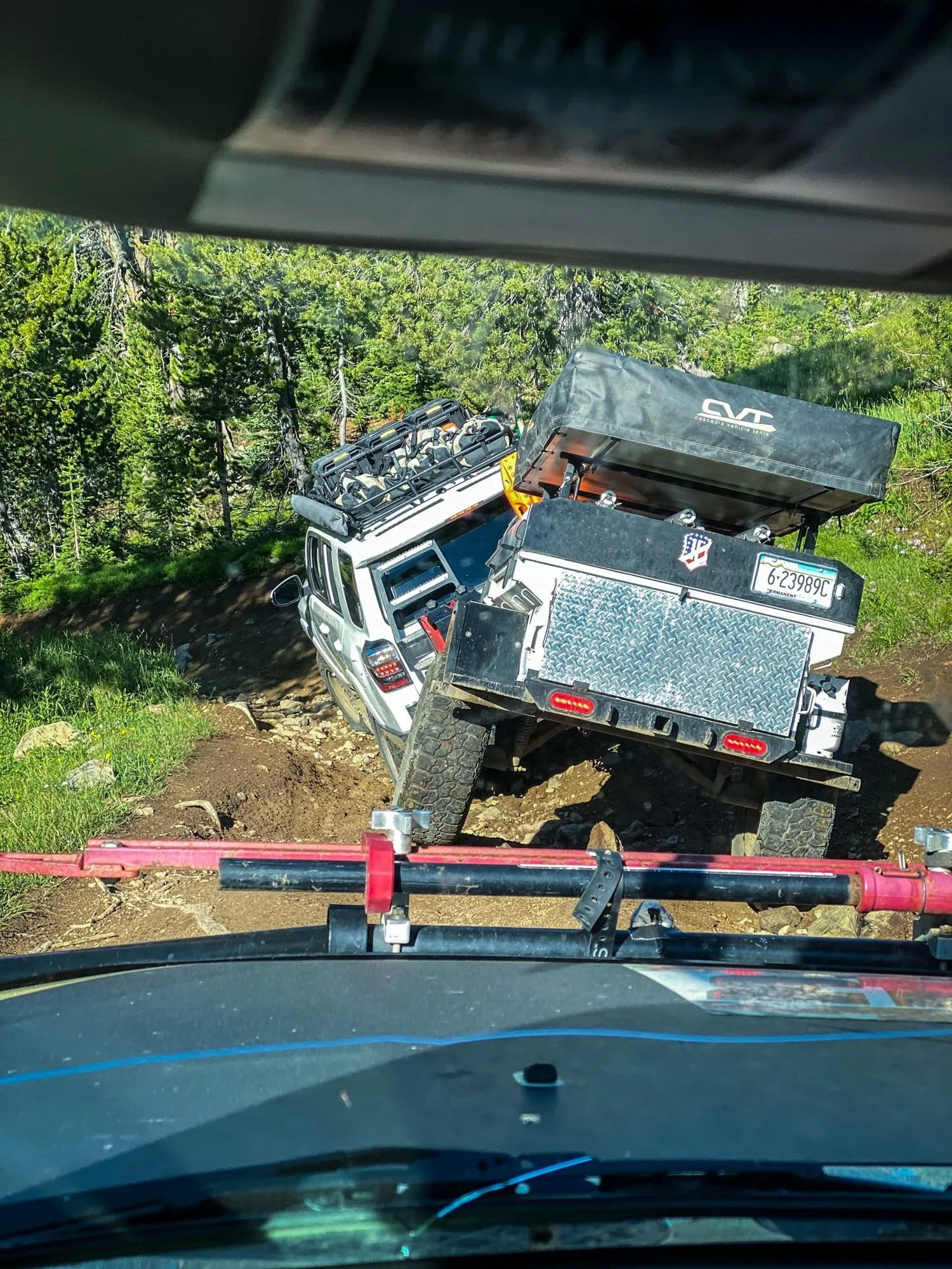 View over a truck hood of an off-road trailer and SUV on a steep, rocky pitch in the trees on the Independence road above the Boulder River, Montana