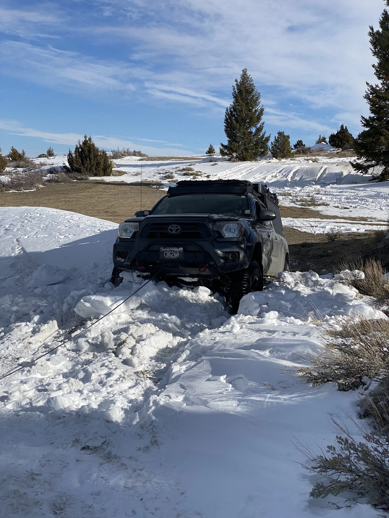 Black Toyota Tacoma buried to the bumper in a snowdrift with a recovery line running from the front during a February snow wheeling run in Montana