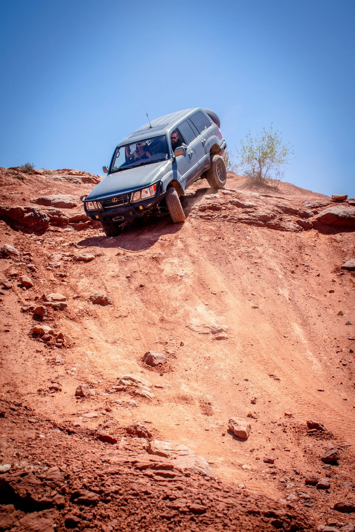 Gray Lexus SUV dropping off the same steep red-rock ledge with its suspension compressed on the Seven Mile Rim trail near Moab, Utah