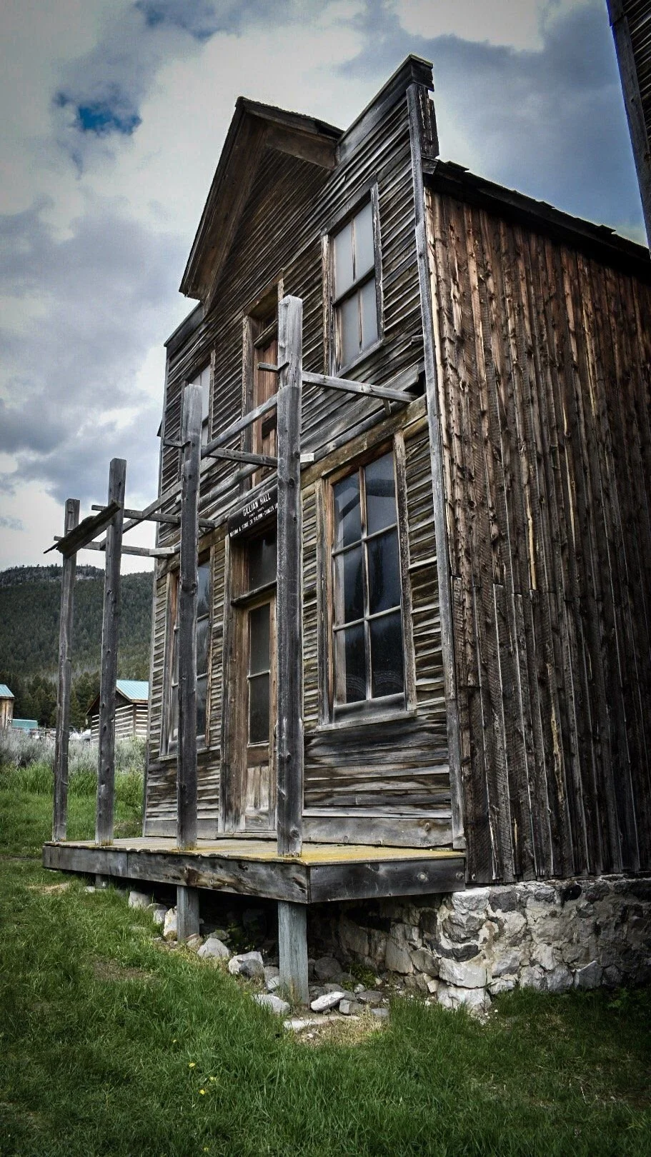 Tall weathered wooden false-front building on a stone foundation under a cloudy sky in the Elkhorn ghost town near Boulder, Montana