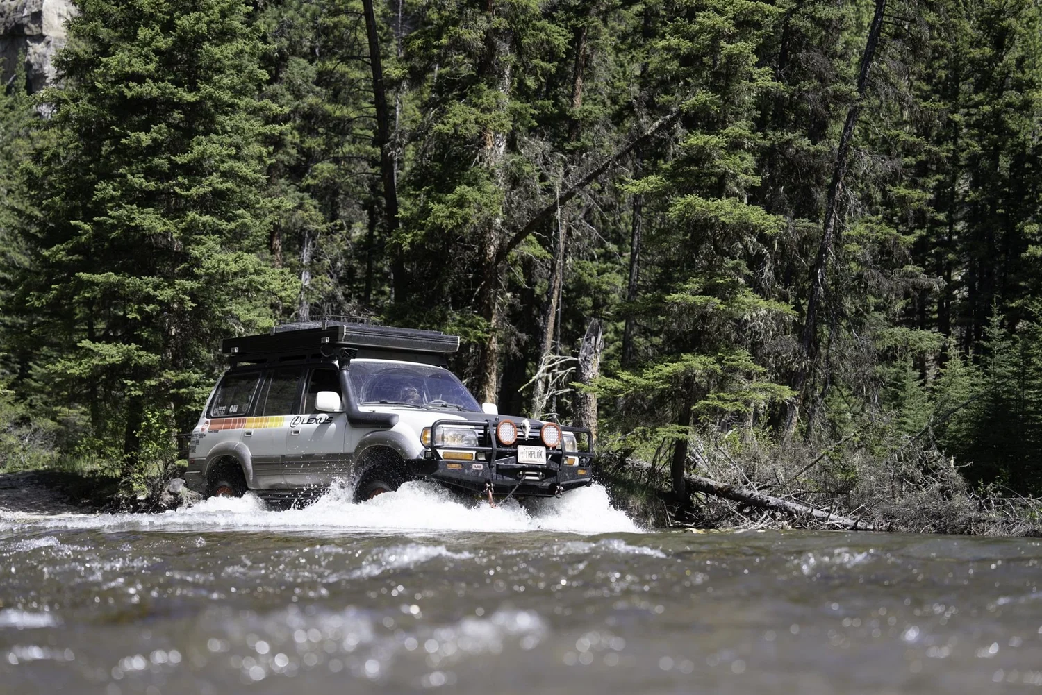 Silver Lexus LX450 with a striped livery, roof rack and snorkel splashing through a river crossing on the Middle Fork Judith River road in the Little Belt Mountains, Montana