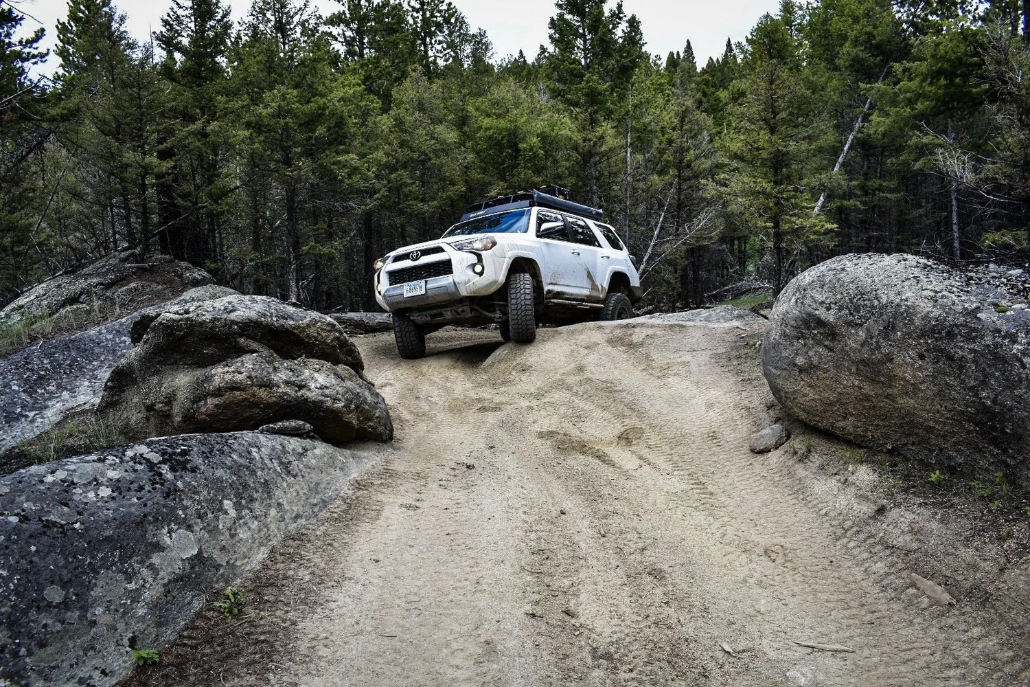 White Toyota 4Runner squeezing between two big granite boulders on a sandy trail on the Ringing Rocks trail near Pipestone, Montana