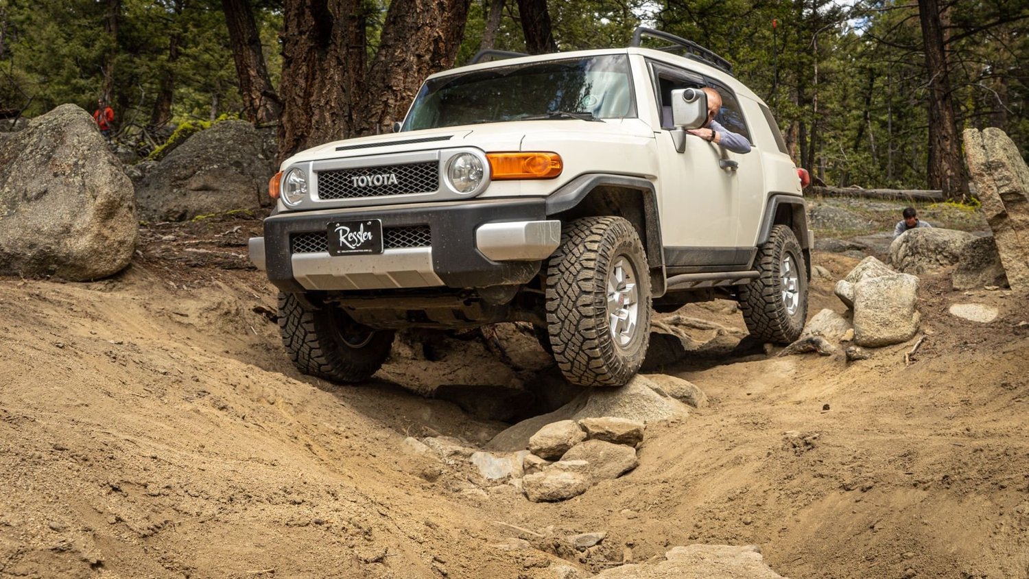 White Toyota FJ Cruiser crawling up a sandy rock step between boulders on the Ringing Rocks trail near Pipestone, Montana
