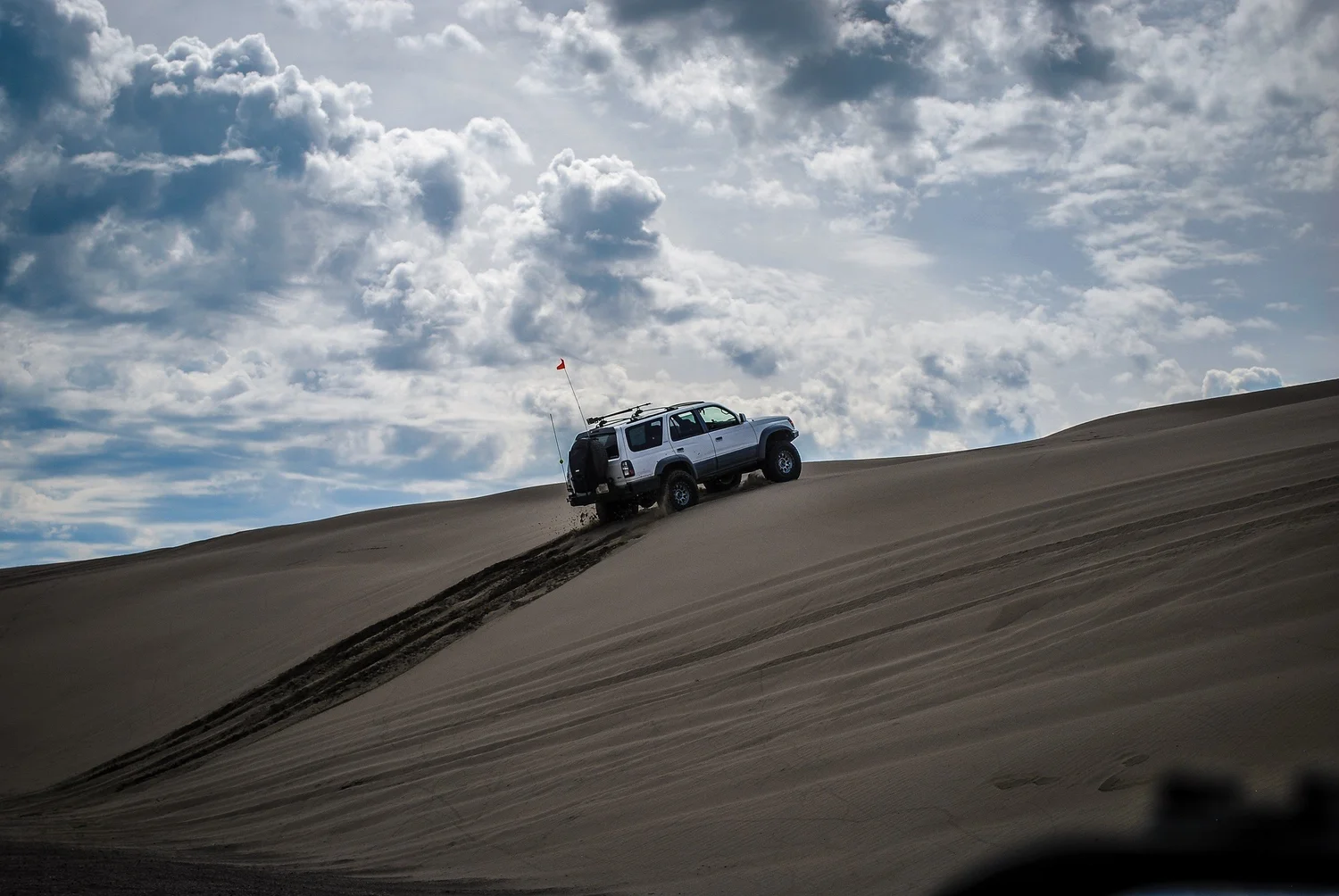 Silver lifted Toyota 4Runner climbing a dune ridge under big clouds at the St. Anthony Sand Dunes in Idaho