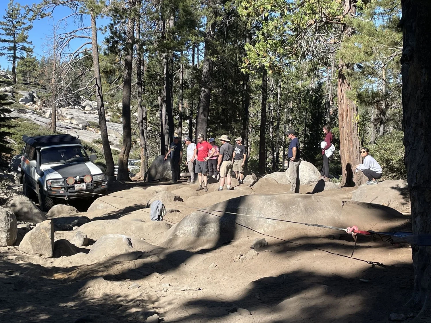 Group of people standing on granite watching a Land Cruiser work through a boulder obstacle in the pines on the Rubicon Trail in California during Rubithon 2022