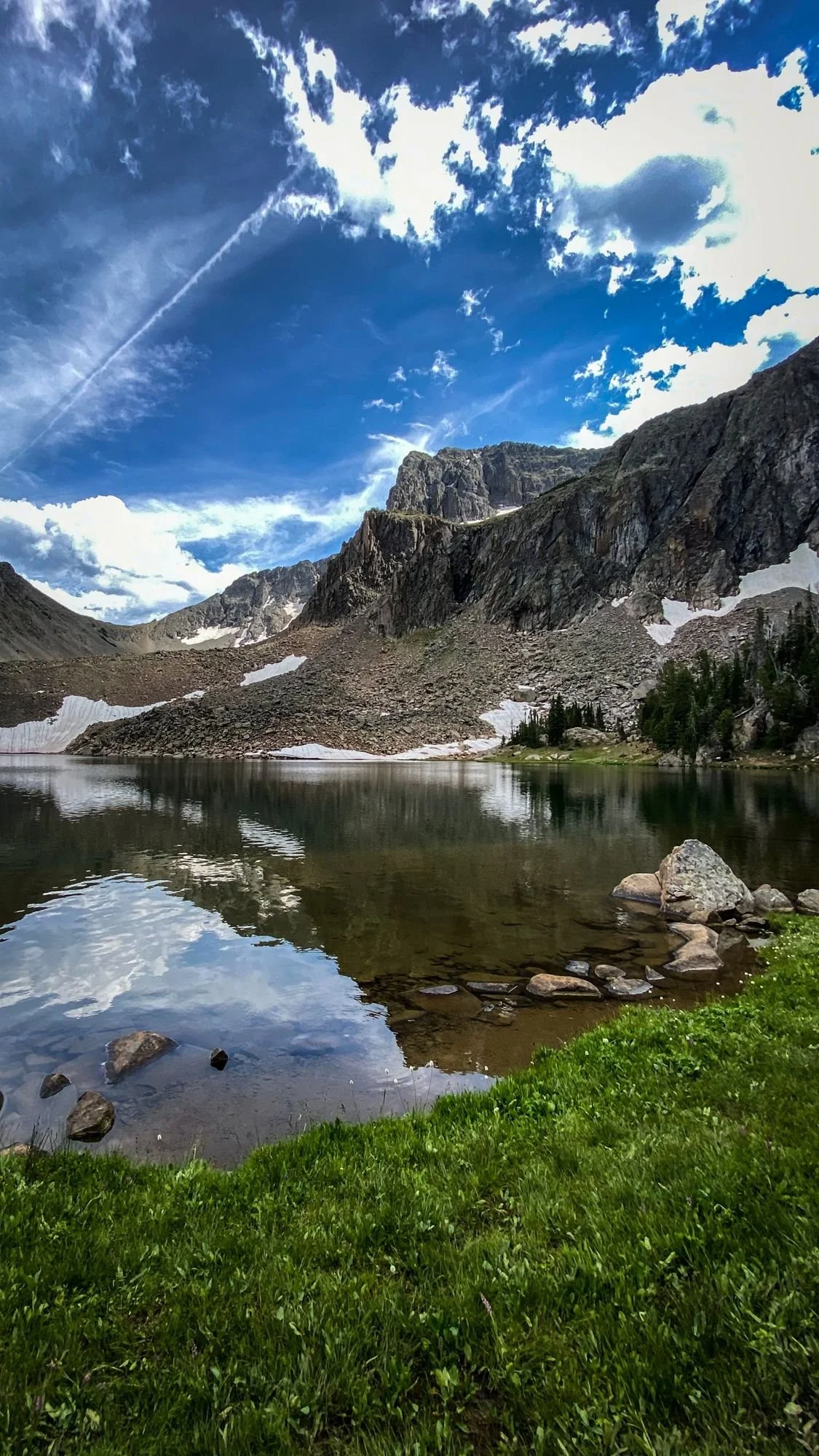 Still alpine lake reflecting rocky peaks and snowfields on the Independence road above the Boulder River, Montana