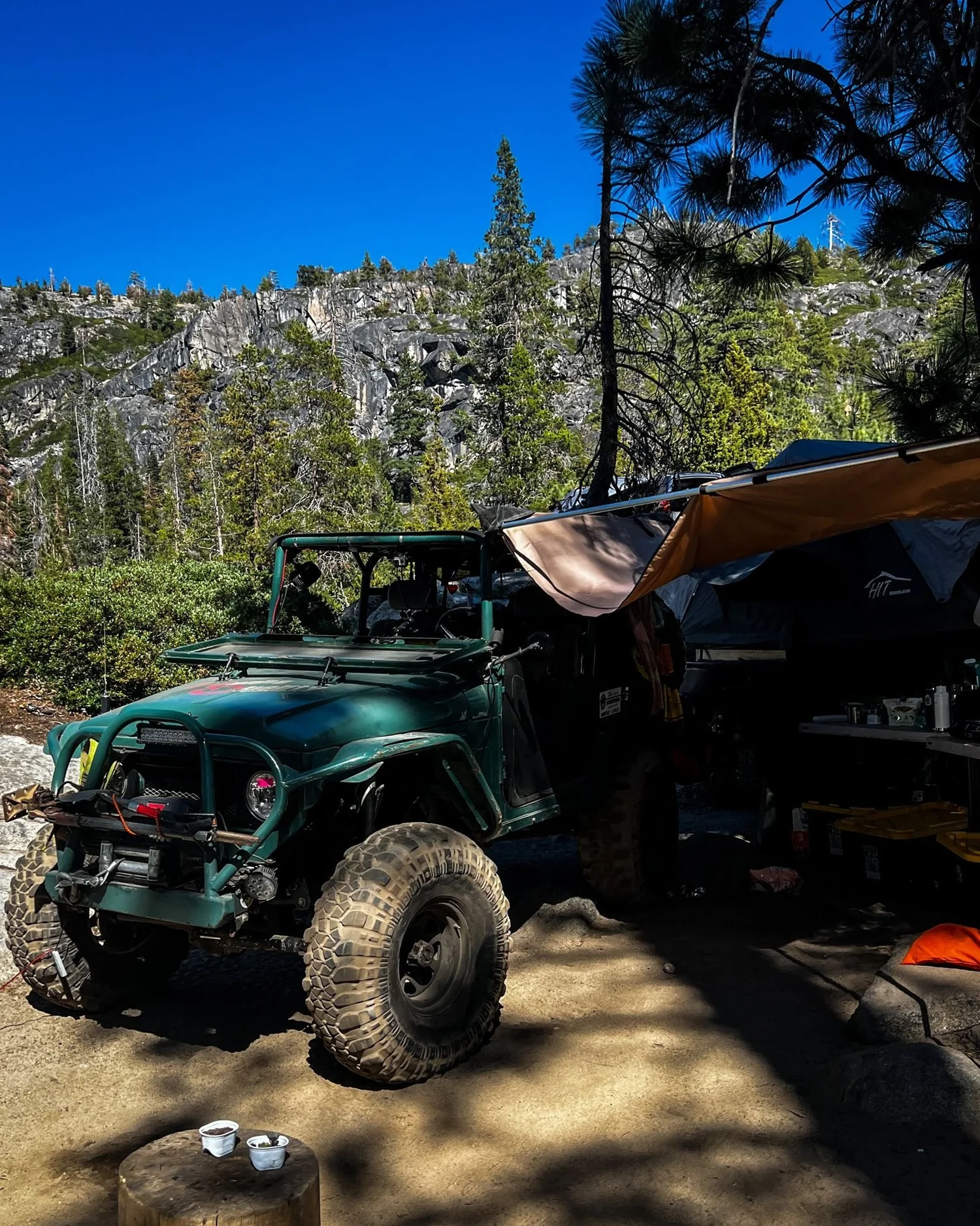 Dark green Land Cruiser with an awning parked at camp below granite cliffs on the Rubicon Trail in California during Rubithon 2022