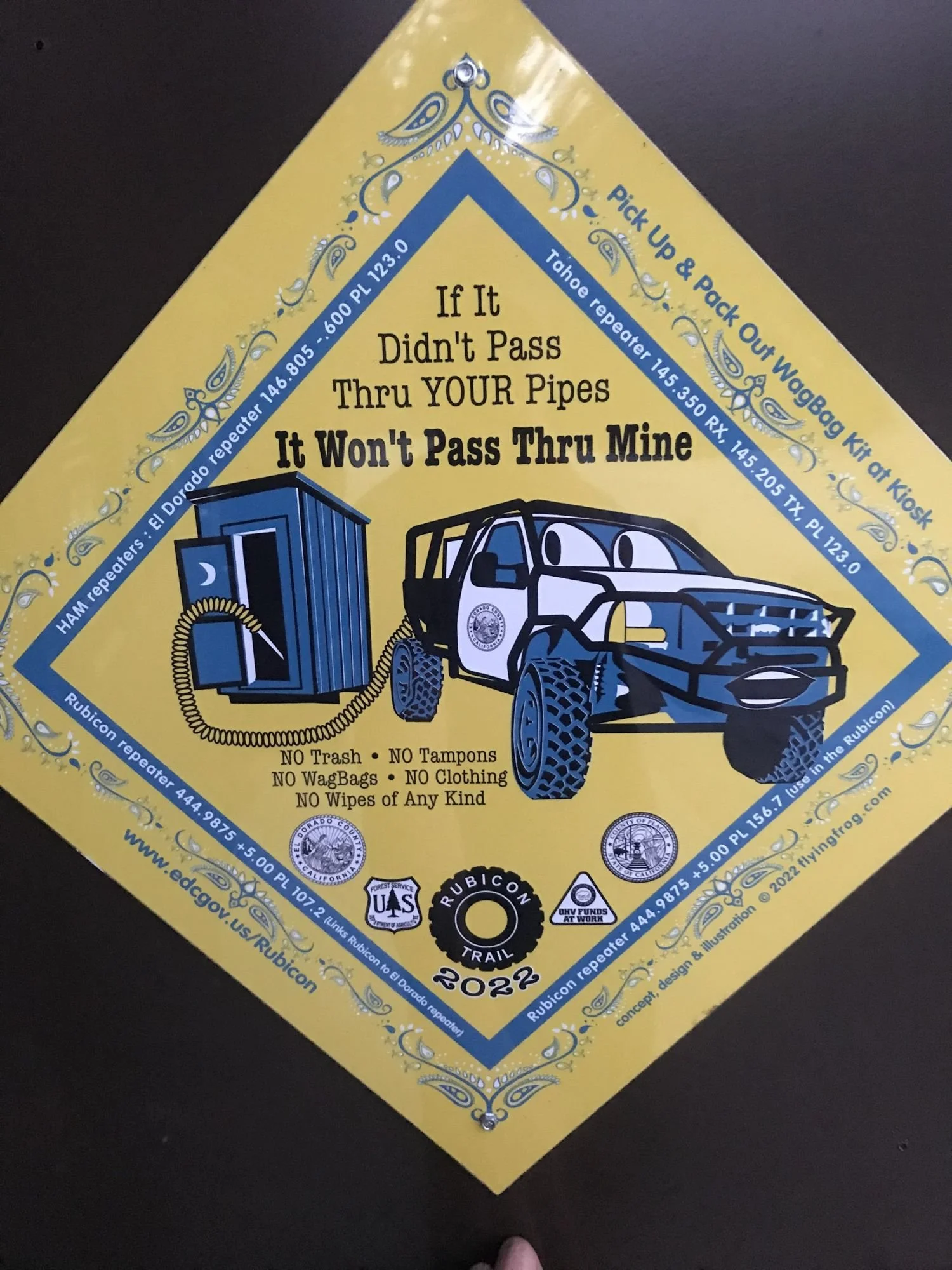 Yellow 2022 Rubicon Trail poster reminding visitors to pack out human waste, with a cartoon outhouse and truck on the Rubicon Trail in California during Rubithon 2022