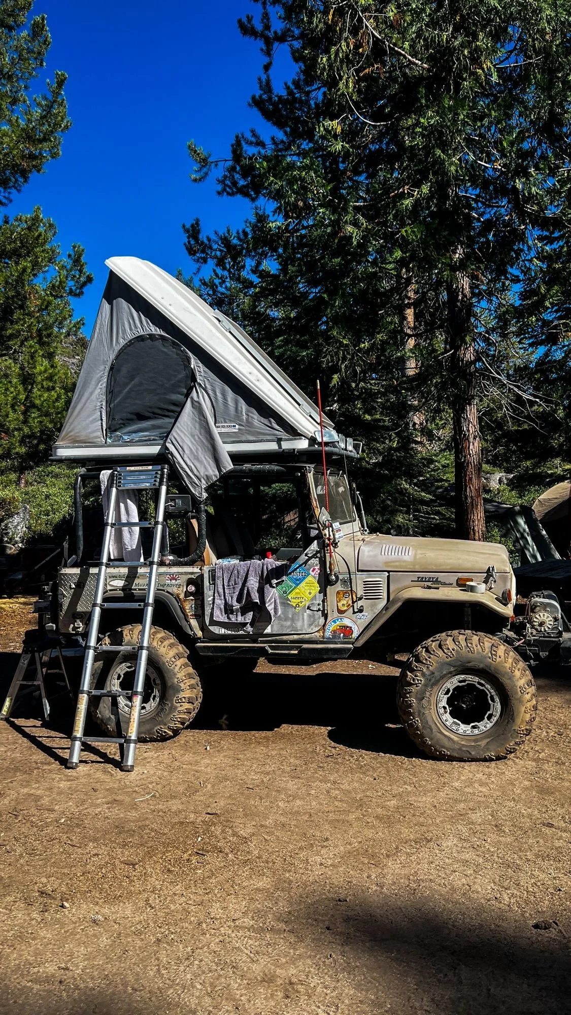 Tan FJ40 with a rooftop tent and ladder in a pine camp on the Rubicon Trail in California during Rubithon 2022