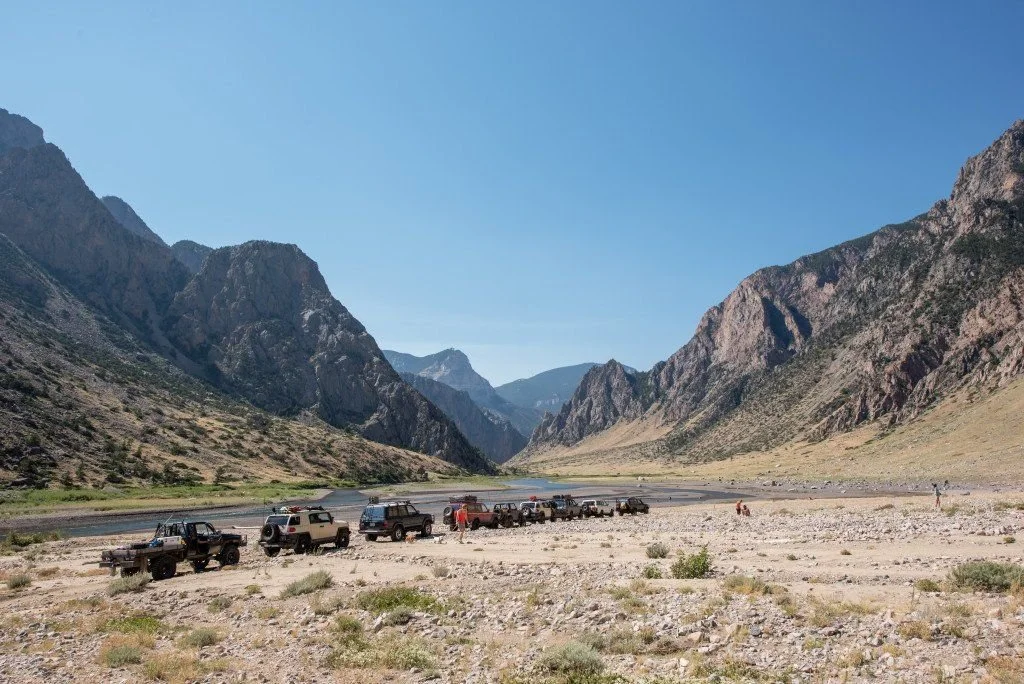 Long line of trucks parked on the gravel canyon floor beside the Clarks Fork below jagged peaks on the Morrison Jeep Trail in Clarks Fork Canyon near Cody, Wyoming