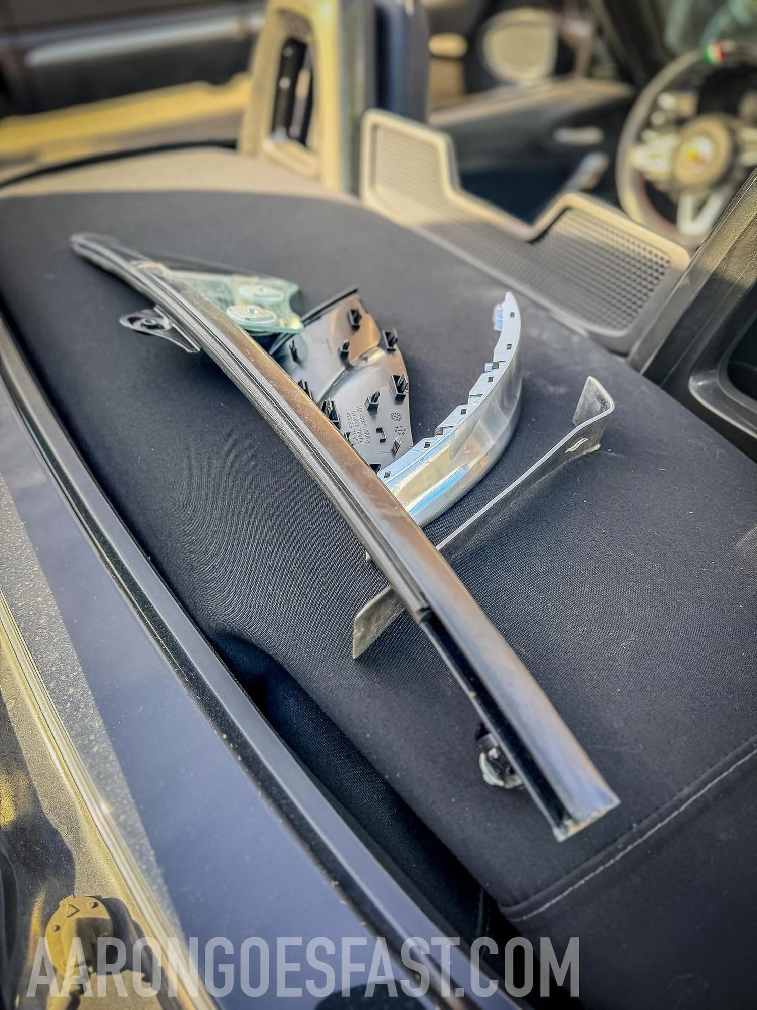 Glass guide, beltline trim and brackets removed from the Fiat 124 door, laid out on the rear deck