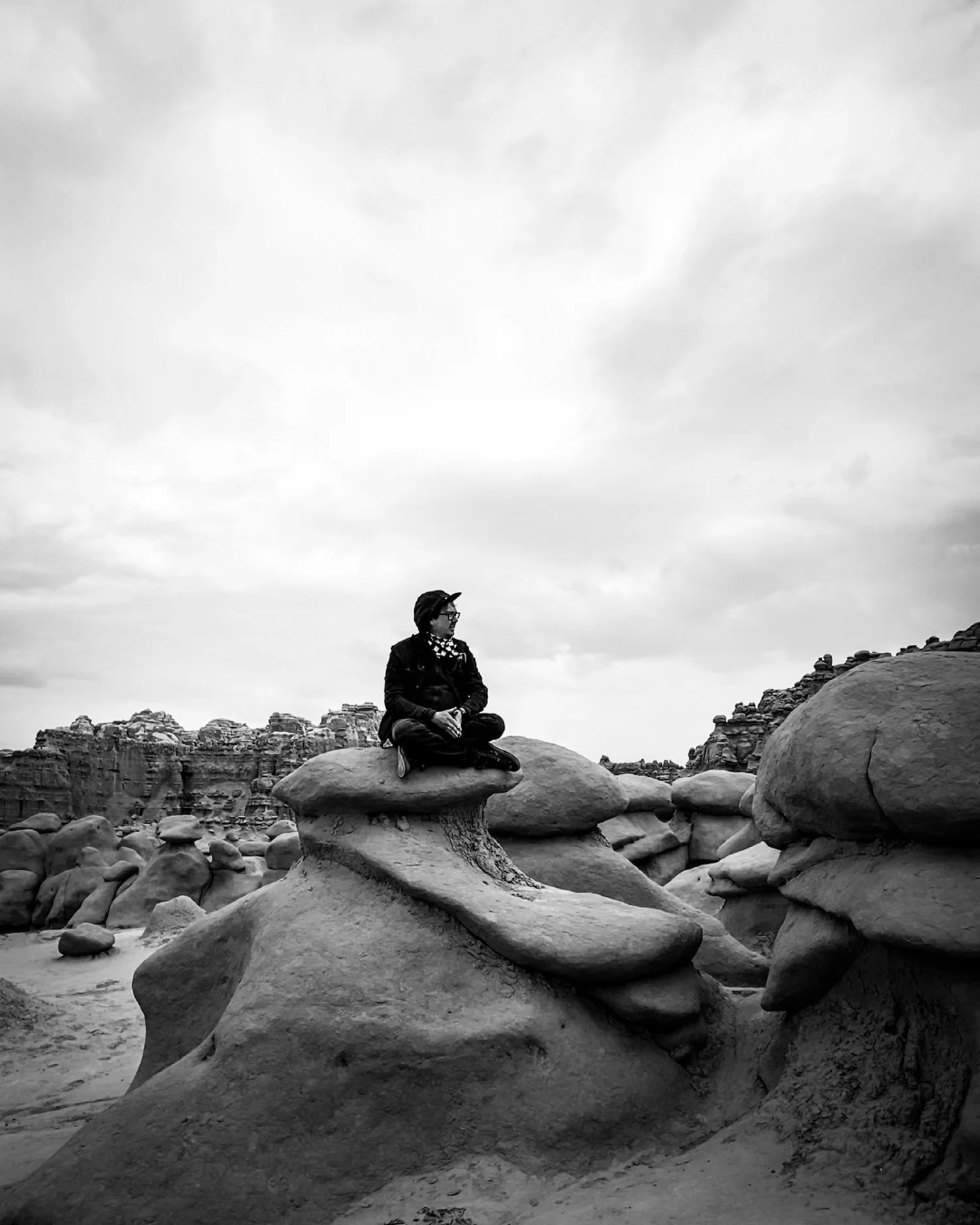 Black and white photo of a person sitting on a rounded hoodoo among goblin-shaped rocks in Goblin Valley State Park, Utah